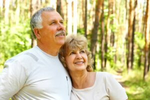 millman law group an older couple hug and smile while standing in a green forest